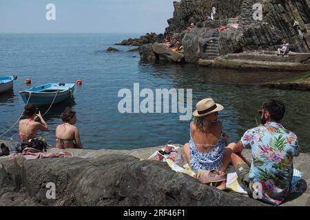 Cinque Terre, Italie - les touristes en maillot de bain prennent le soleil au quai de Riomaggiore. Ville balnéaire sur la Riviera italienne. Les gens sur une plage rocheuse sous le soleil. Summ Banque D'Images