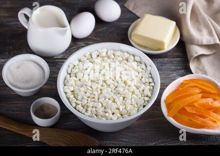 Bol avec fromage cottage, oranges confites, crème, oeufs, beurre, sucre, sucre vanillé sur un fond en bois. Ingrédients pour la cuisson maison. Banque D'Images