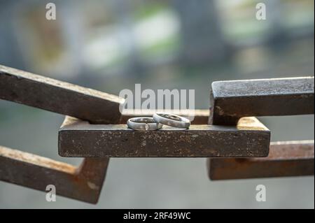 Deux mains avec des anneaux de mariage reposent sur une chaîne d'ancrage solide. Banque D'Images