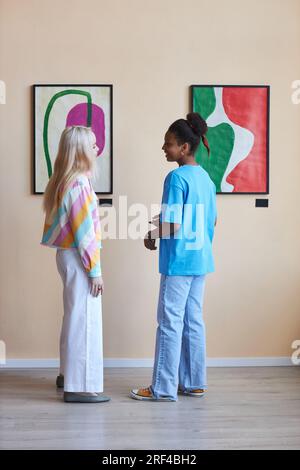 Portrait vertical pleine longueur de deux adolescentes discutant des images dans la galerie d'art moderne Banque D'Images