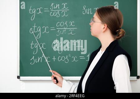 Jeune professeur de mathématiques avec pointeur près du tableau noir dans la salle de classe Banque D'Images