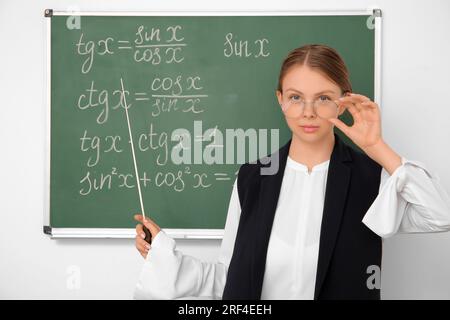 Jeune professeur de mathématiques avec pointeur près du tableau noir dans la salle de classe Banque D'Images