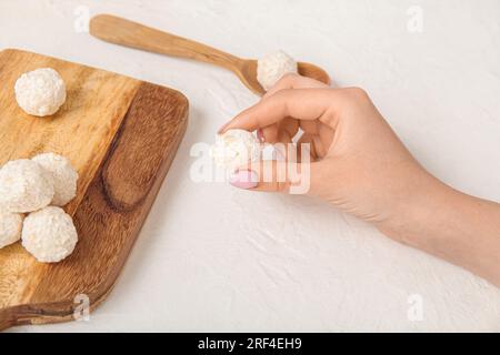 Femme prenant des bonbons à la noix de coco savoureux de la planche sur la table blanche Banque D'Images