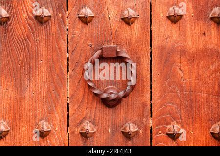 Un ancien heurtoir en fer orné sur une vieille porte d'entrée en bois. Détail extérieur rouillé torsadé Banque D'Images