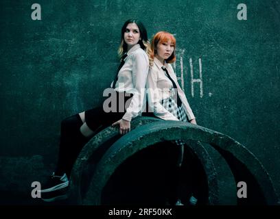 Deux beaux étudiants mignons en uniforme posent sur des anneaux de béton sur le fond d'un vieux mur de béton sombre. Grunge et ville industrielle. CONSTRU Banque D'Images
