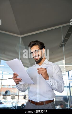 Heureux jeune homme d'affaires latin vérifiant les documents financiers dans le bureau. Banque D'Images