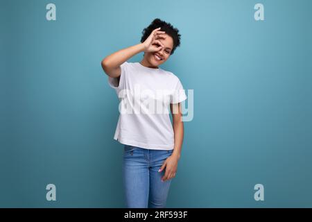 surprise jeune femme brune avec cheveux afro dans un t-shirt blanc utilise ses mains pour la gesticulation et la communication Banque D'Images