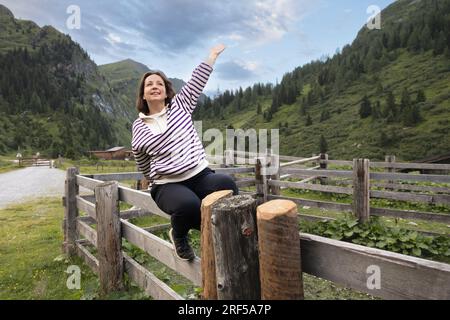 Jeune femme avec le sourire assis sur la clôture et regardant vers le haut, levant la tête, le concept de l'unité avec la nature, l'écotourisme Banque D'Images