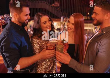 Des amis heureux qui siègent des verres avec des cocktails frais au bar Banque D'Images