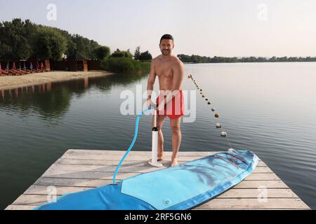 Homme pompant la planche de SUP sur la jetée Banque D'Images
