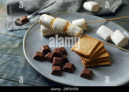 Ingrédients pour un délicieux sandwich avec des guimauves rôties et du chocolat sur une table en bois gris, closeup Banque D'Images