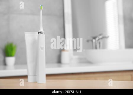 Brosse à dents électrique et tube avec pâte sur table en bois dans la salle de bain. Espace pour le texte Banque D'Images