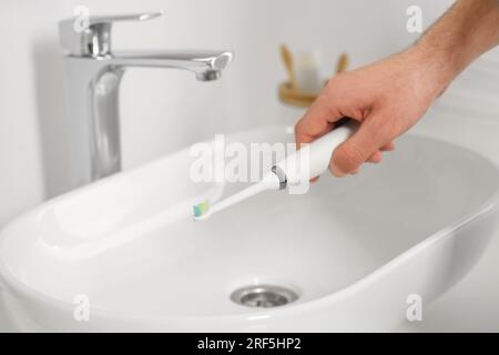 Homme tenant une brosse à dents électrique au-dessus de l'évier dans la salle de bains, gros plan Banque D'Images