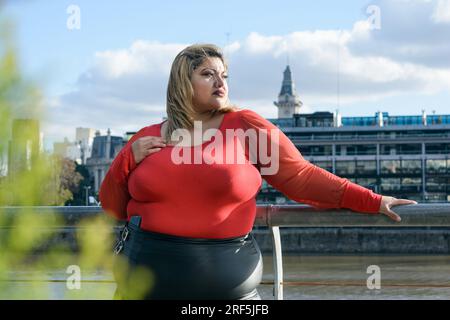 Portrait de jeune femme latine de taille plus tendance dans des vêtements rouges, à l'extérieur avec des bâtiments en arrière-plan à Puerto Madero Buenos Aires, debout à la recherche t Banque D'Images