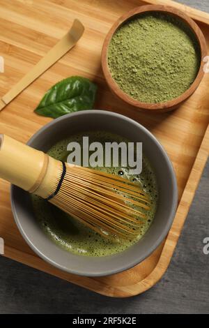 Tasse de thé matcha frais avec fouet en bambou, poudre verte et cuillère sur la table gris foncé, vue de dessus Banque D'Images