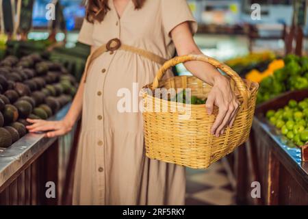 Une femme enceinte brillante après quarante ans fait un choix sain en sélectionnant des légumes et des fruits biologiques sur le marché biologique dynamique, en donnant la priorité Banque D'Images