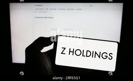 Personne tenant le téléphone mobile avec le logo de la société japonaise Z Holdings Corporation sur l'écran devant la page Web d'affaires. Concentrez-vous sur l'affichage du téléphone. Banque D'Images