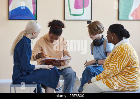 Groupe diversifié d'adolescents assis en cercle et tenant des livres tout en discutant de conférences d'art dans la galerie d'art moderne ou le musée Banque D'Images