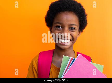 Portrait d'écolier biracial heureux avec des livres portant un tshirt jaune sur fond orange Banque D'Images