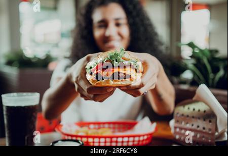 Fille souriante montrant un hamburger dans un restaurant. Gros plan d'une femme montrant un hamburger appétissant dans un restaurant Banque D'Images