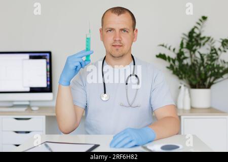 Portrait d'un homme médecin portant un uniforme médical avec seringue à la main assis à la table à l'hôpital Banque D'Images