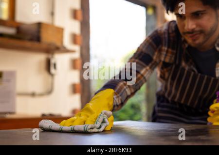 Homme indien portant des gants jaunes et le plan de travail de nettoyage dans la cuisine, espace de copie Banque D'Images