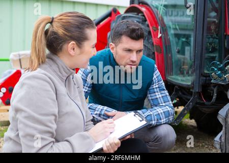 mécanicien féminin avec presse-papiers regardant le tracteur Banque D'Images