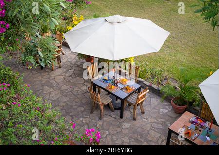 Murchison Falls National Park, Ouganda - 7 juin 2022 : une petite table à manger sous un parasol sur une terrasse tropicale en Ouganda Banque D'Images