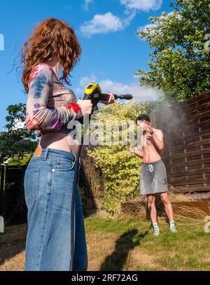 Amusement d'été, fille aspergeant garçon avec pistolet à eau Banque D'Images