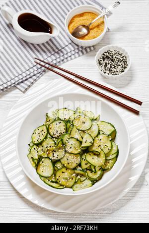 Sunomono, salade japonaise de concombres, tranches de concombres avec sauce asiatique de soja, vinaigre de riz, huile de sésame et sucre dans un bol blanc avec baguettes Banque D'Images