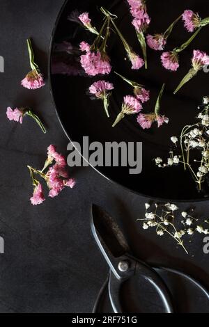 Assiette avec des fleurs séchées et des ciseaux sur fond noir - sombre et moody Banque D'Images
