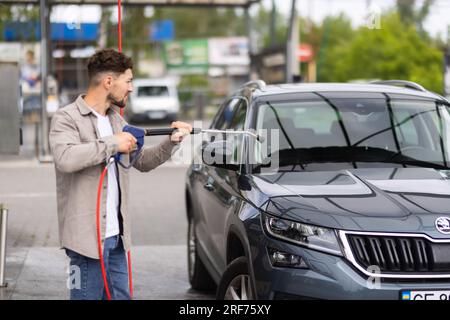 L'homme lave sa voiture sous l'eau sous pression à l'extérieur Banque D'Images