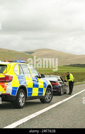 Agent de la police de la circulation parlant au conducteur d'une voiture bmw noire qui a été faite pour s'arrêter sur l'épaule dure de l'autoroute M74 Écosse, Royaume-Uni Banque D'Images