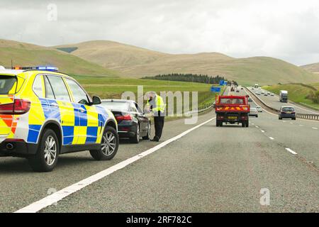 Agent de la police de la circulation parlant au conducteur d'une voiture bmw noire qui a été faite pour s'arrêter sur l'épaule dure de l'autoroute M74 Écosse, Royaume-Uni Banque D'Images