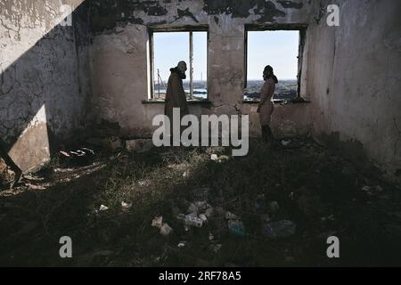 Deux personnes, un gars et une fille en masques à gaz, se tiennent dans une maison abandonnée à côté de la fenêtre et regardent en arrière, apocalypse Banque D'Images