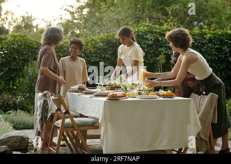 L'un des deux frères afro-américains aidant à servir la table pour le dîner en plein air dans le jardin tandis qu'un autre parle à sa grand-mère Banque D'Images