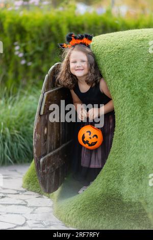 Une petite fille mignonne dans un costume de sorcière pour Halloween se promène dans le parc dans un panier de bonbons en forme de citrouille Banque D'Images