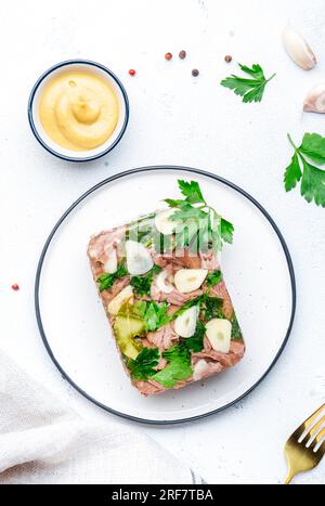 Viande aspic d'hiver, bœuf bouilli froid dans un bouillon de gelée épicé sur assiette avec ail et vinaigrette à la moutarde de dijon. Fond de table blanc, vue de dessus Banque D'Images