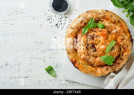 Délicieuse tarte Spanakopita avec fromage feta doux et épinards sur de vieux fonds de table en bois blanc. Tarte à pâtisserie filo grecque traditionnelle Spiral spanakopit Banque D'Images