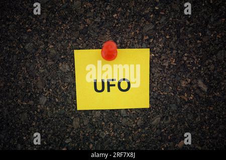 Une note de papier jaune avec l'abréviation UFO dessus épinglée à un panneau de liège. Gros plan. Banque D'Images