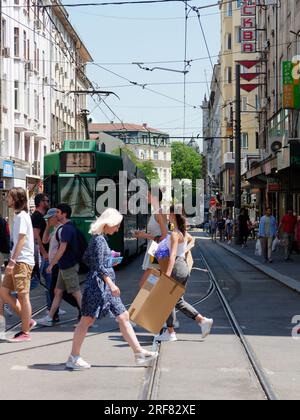 Les gens traversent la route devant un tramway vert aka Streetcar aka Trolley dans une rue de la ville de Sofia, Bulgarie. 01 août 2023. Banque D'Images