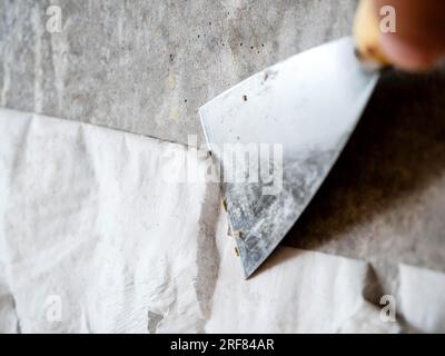Le vieux papier peint en papier est retiré du mur de béton avec une spatule. Vieux murs. Banque D'Images