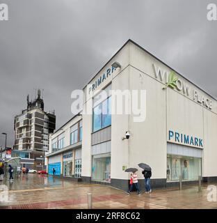 Deux acheteurs avec parapluies passent devant la boutique Primark dans le centre-ville de Corby, en Angleterre, un jour d'été pluvieux, le 2023 juillet. Banque D'Images