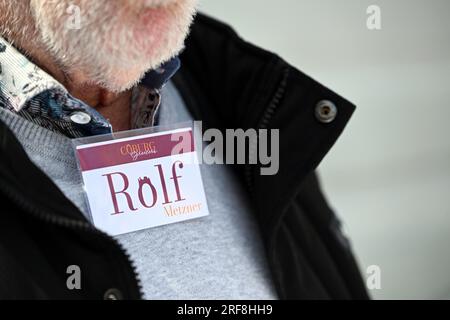 Coburg, Allemagne. 17 mai 2023. Un panneau avec le logo Coburg Greeters identifie Rolf Metzner comme un guide touristique. Dans sa main, il tient un dossier avec des photos historiques. Dans de petites promenades personnelles - ce que l'on appelle des «saluts» - les habitants guident volontairement les visiteurs à travers leur ville sur demande. Crédit : Pia Bayer/dpa/Alamy Live News Banque D'Images