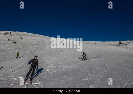 Falcade, Italie - 15 février 2023 : piste de ski avec skieur sous ciel bleu. Les gens descendent les montagnes enneigées à skis. Groupe de skieurs sur une piste de ski Banque D'Images