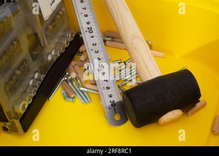 Jeu de tournevis, règle métallique, maillet, vis pour meubles, chevilles en bois dans un récipient jaune Banque D'Images