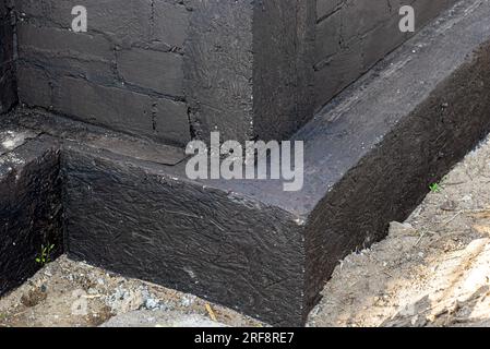 Semelles en blocs de béton peintes avec masse asphalte-caoutchouc de dispersion noire, piliers en béton armé visibles. Banque D'Images