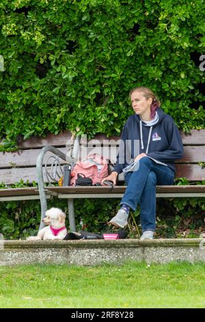 dame assise sur un banc de parc avec un petit chien terrier à côté d'elle sur l'herbe. Banque D'Images