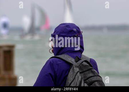 spectateur de la semaine cowes sur une journée humide et venteuse. femme portant un imperméable regardant les yachts à la régate annuelle cowes week sur l'île de wight. pluvieux. Banque D'Images