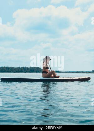 belle femme assise sur le supboard pagayant au milieu du lac Banque D'Images